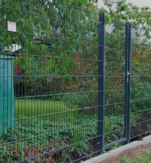 Schwarzer Gitterzaun mit einem Zugangstor in einem Garten 